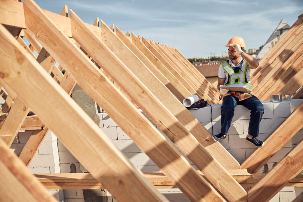 Hard-working builder sitting near a wooden roof frame